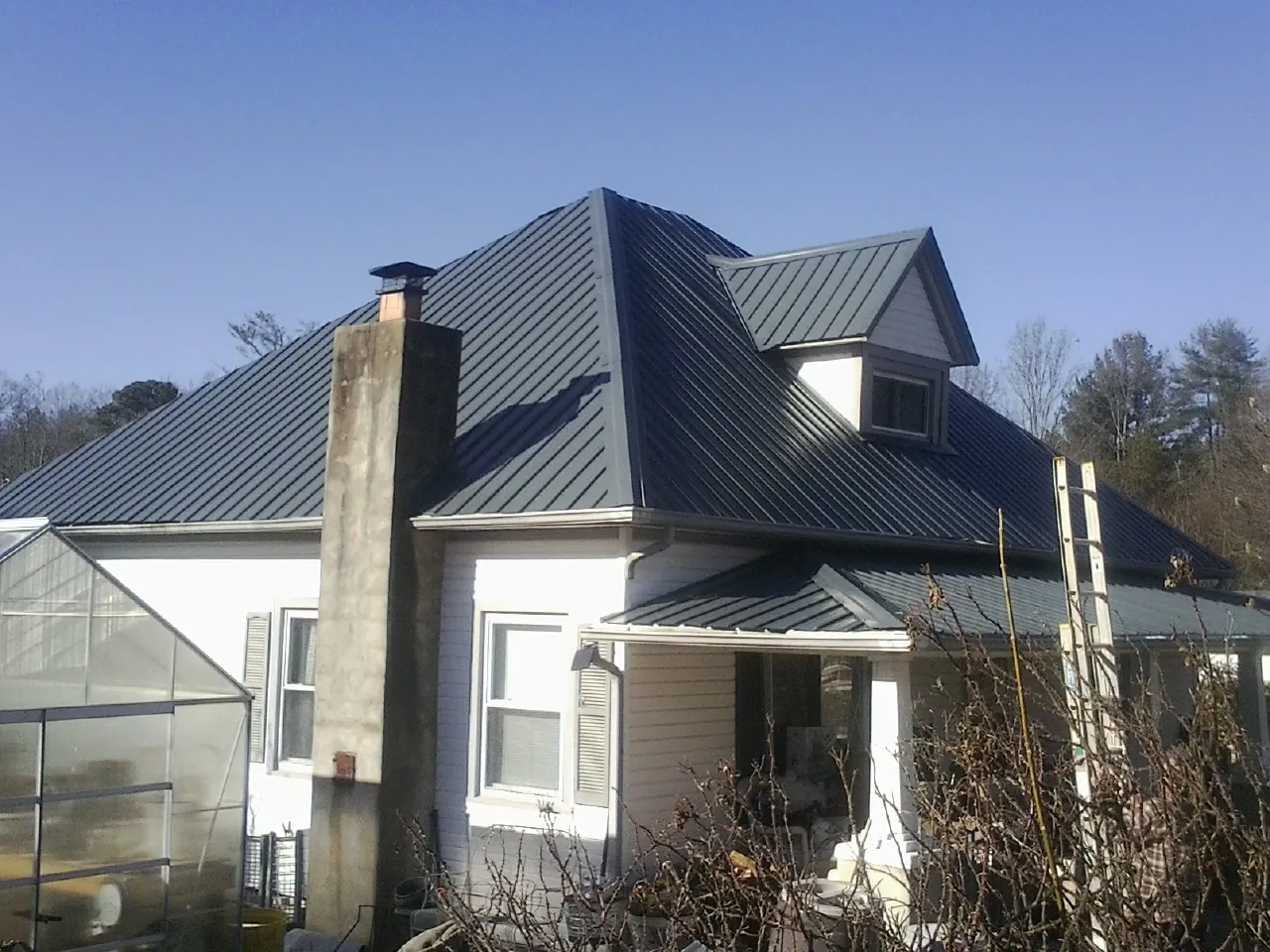 Dark blue standing seam metal roof on a white farmhouse with dormer — Slate & Tile Roof Repair by Roofing Brothers in Normangee