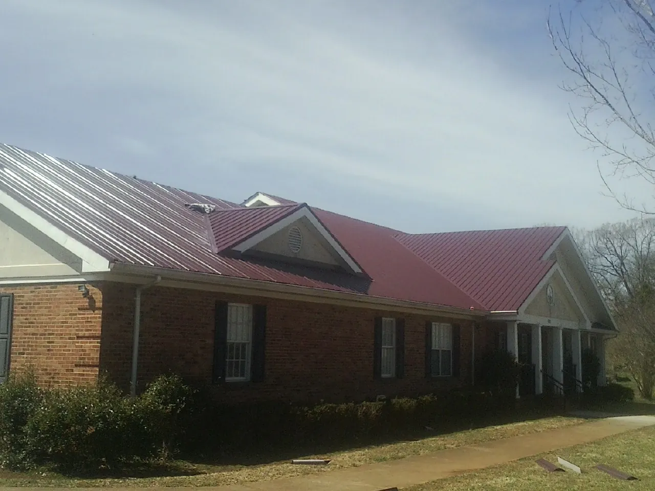 Red metal roof with gabled entries on a long brick building, from a Hail Damage Roof Repair job in Normangee