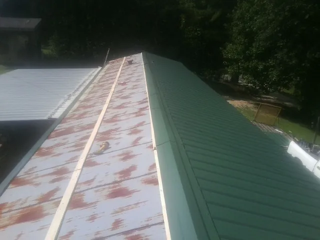 Old rusted panels beside newly installed green metal roofing — Wind Damage Roof Repair by Roofing Brothers in Normangee