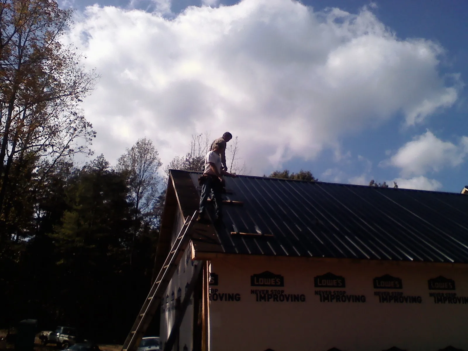 Roofer fastening dark metal panels high against a cloudy sky, from a Roof Inspection job in Normangee