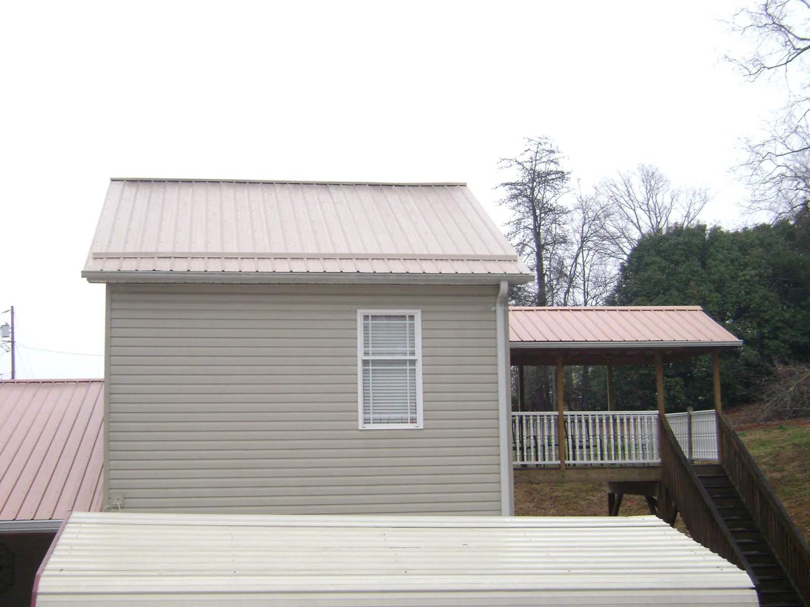 Tan metal roofs on a two story addition and attached porch, from a Roof Replacement job in Normangee